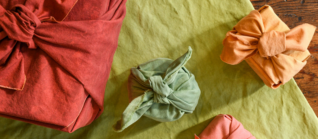 Upcycled, hand-dyed, and reusable gift wrapping textiles called furoshiki wraps in red, green, pink and clementine orange.