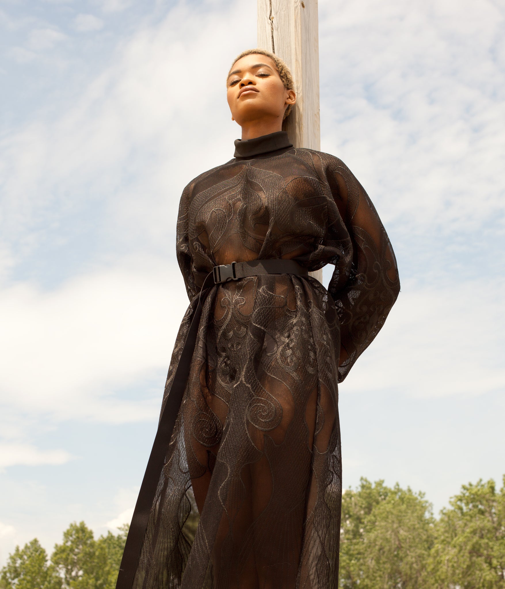 photo of model leaning against a wooden pole while wearing the House of Glass Hot Mesh Dress