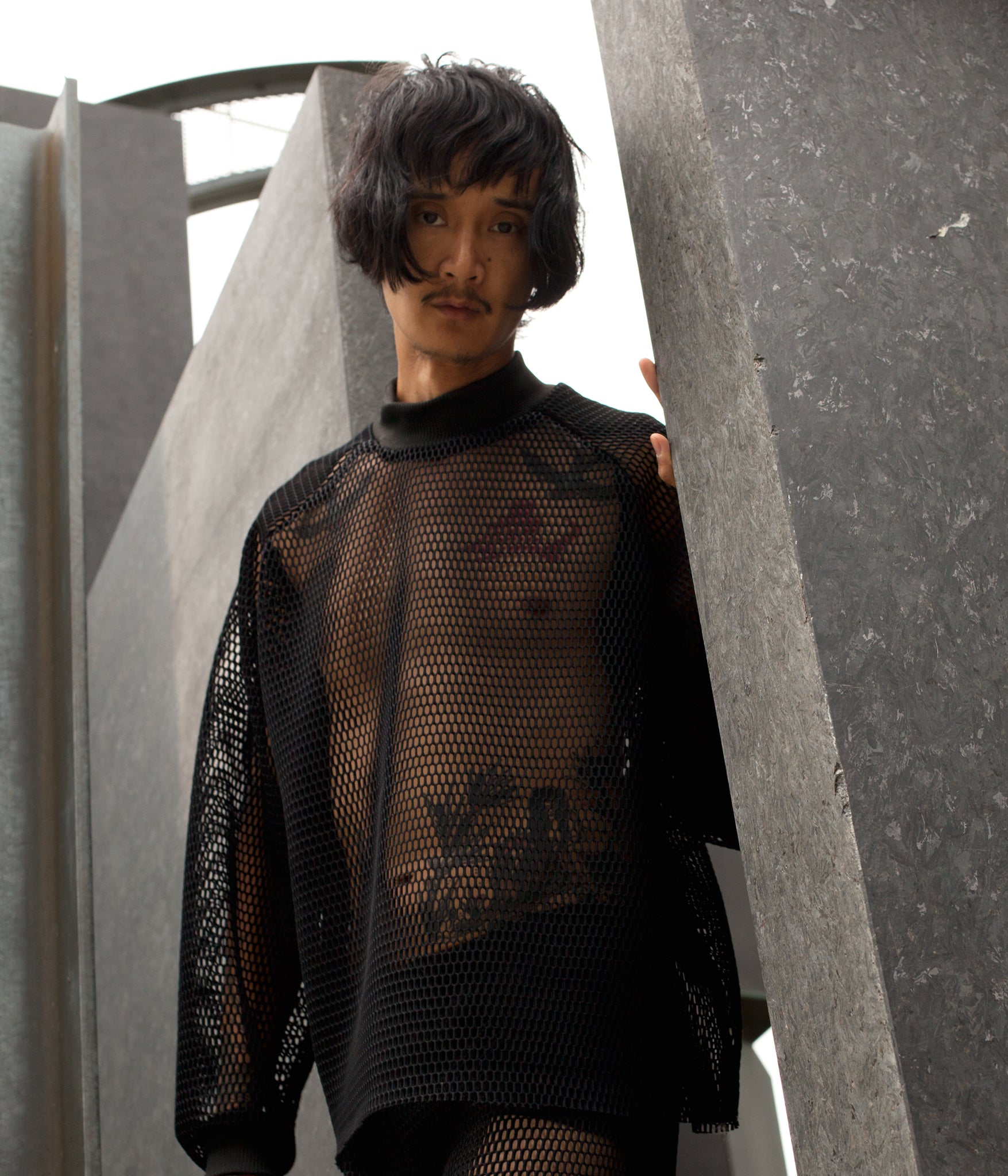 picture of model wearing House of Glass Hot Mesh Tracksuit standing in granite sculpture looking down into the camera