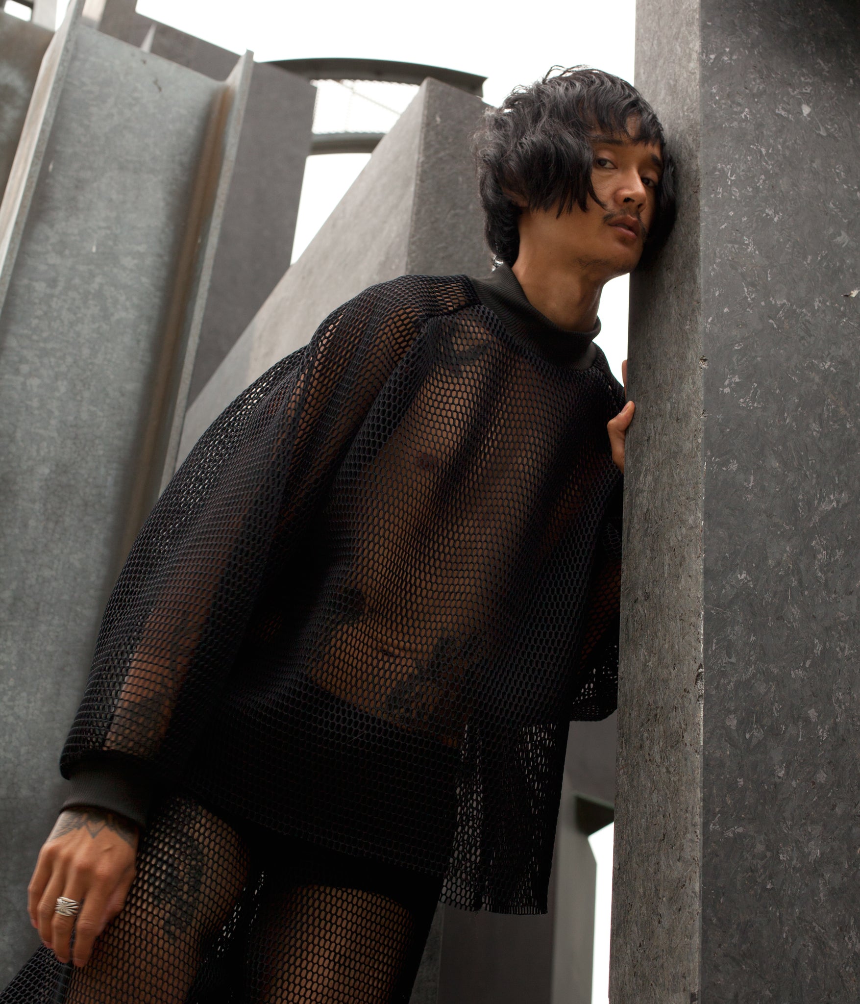 model standing in granite sculpture while wearing the House of Glass Hot Mesh Tracksuit and looking down into the camera