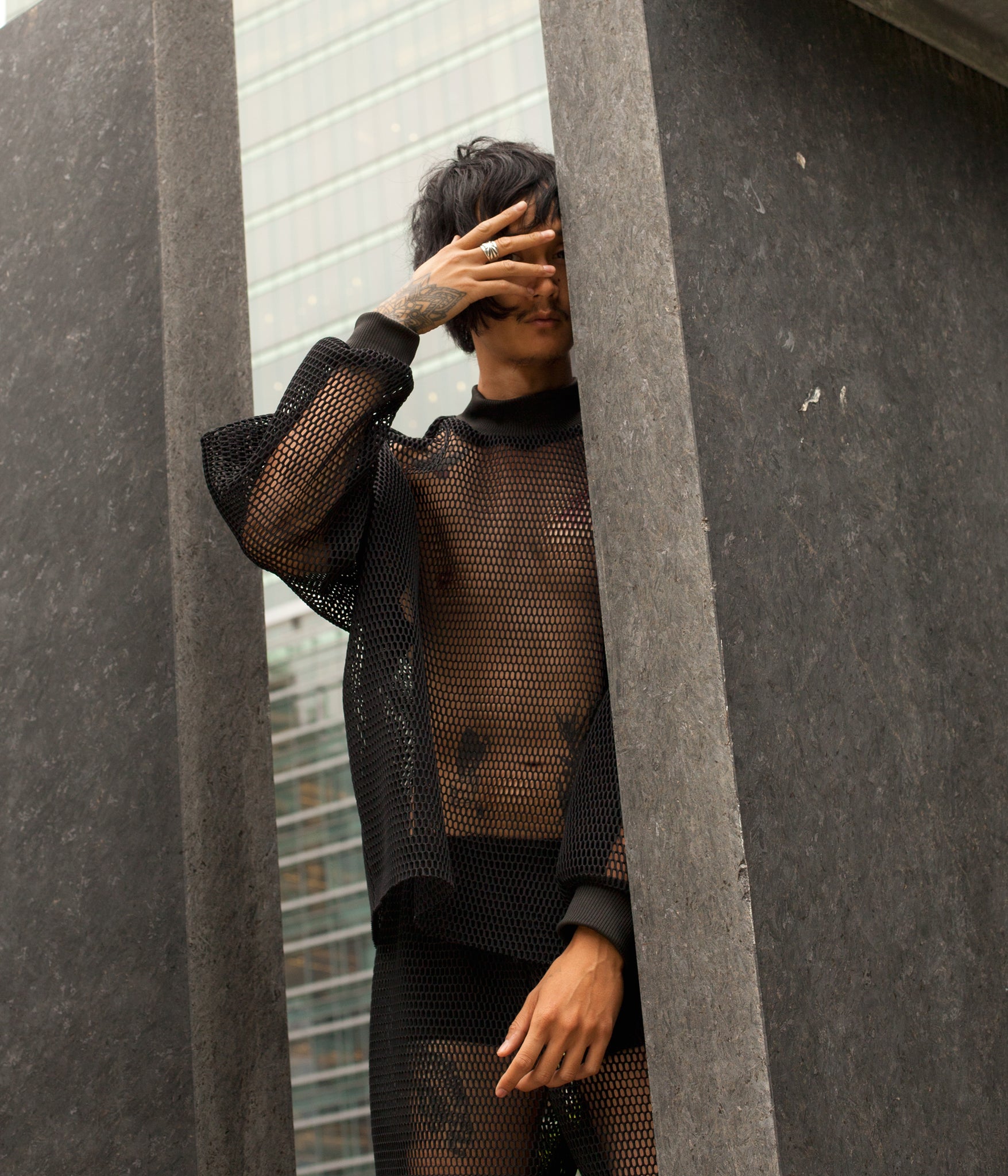 model standing amidst a granite sculpture wearing the House of Glass Hot Mesh Tracksuit and looking out at the camera from behind their fingers