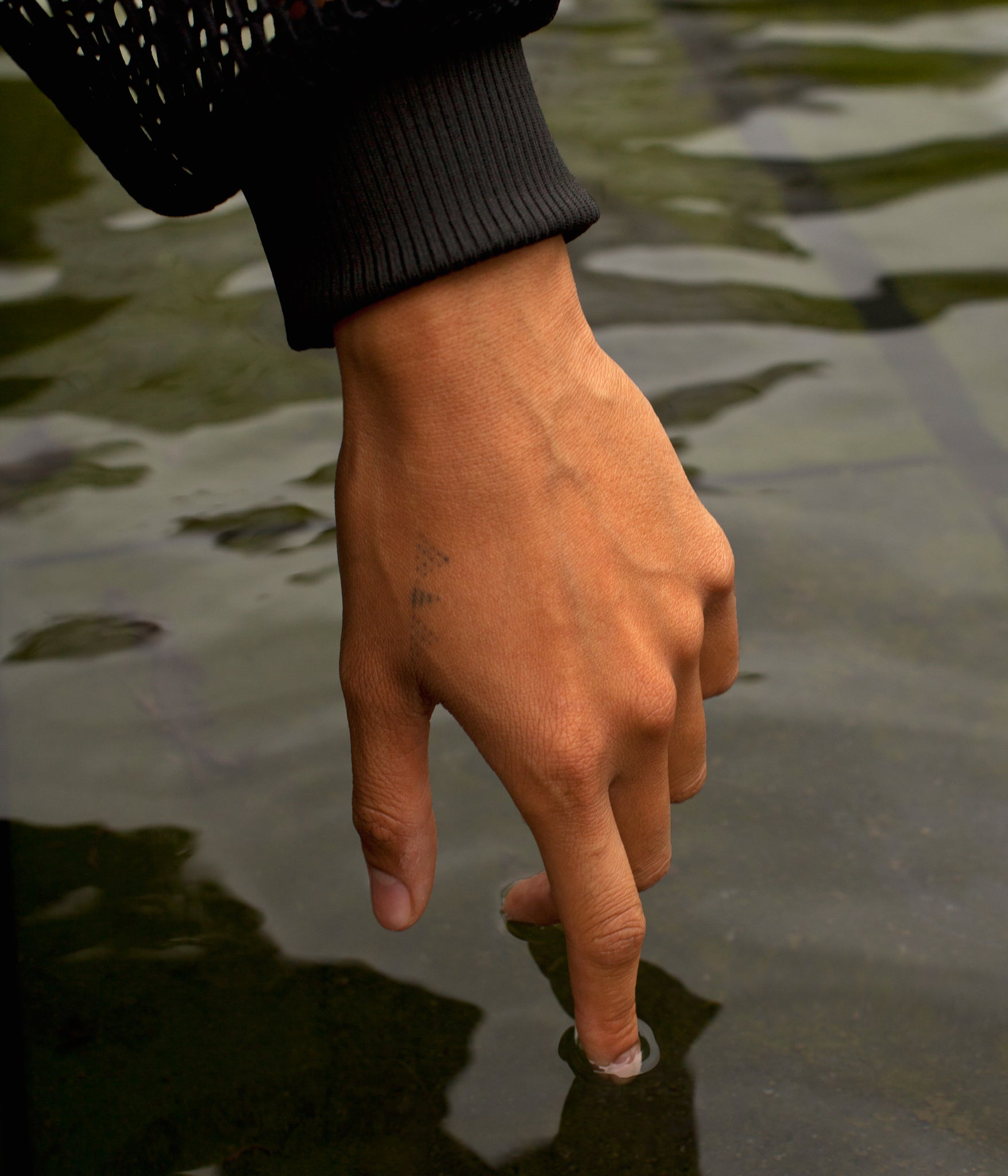 close up picture of model's hand reaching into a body of water