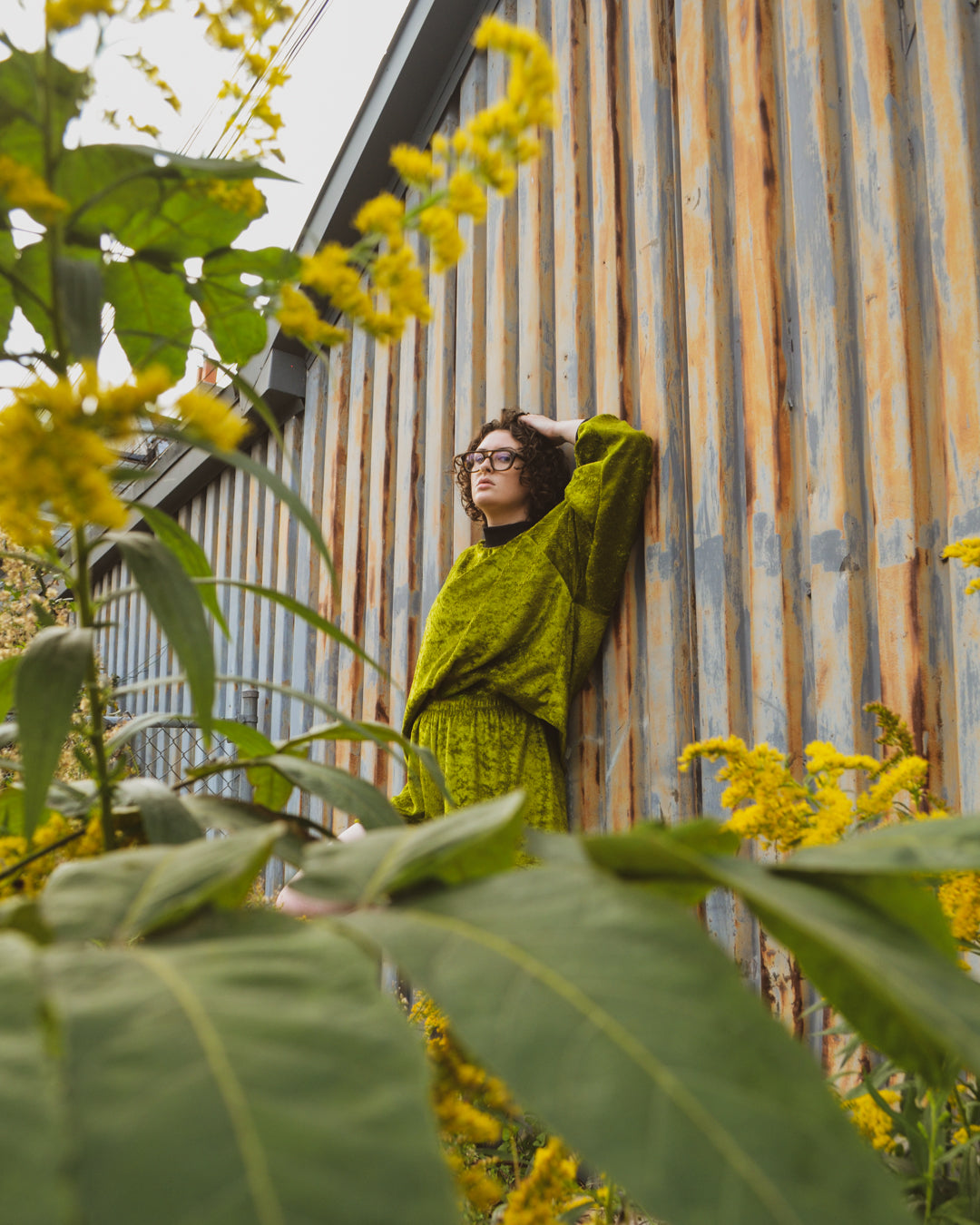 photograph taken through some plants of non binary model wearing the House of Glass Oscar Half Suit