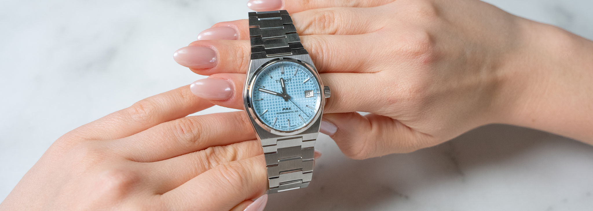 Tissot PRX Watch on woman model hands with white marble background by Orly Jewellers. Photo Credits : Solia Numérique Inc.