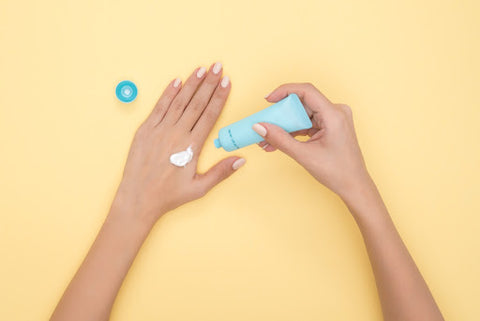 Person applying white sunscreen cream from light blue tube on the back of another hand against pale yellow background, for Ivy Leaf Skincare blog