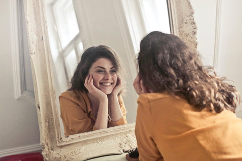 Woman with face in her hands smiling at her reflection, for Ivy Leaf Skincare blog