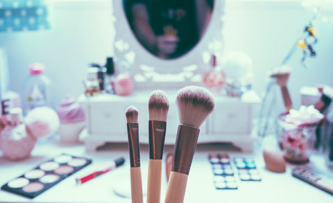 3 makeup brushes held in front of beauty vanity, for Ivy Leaf Skincare blog