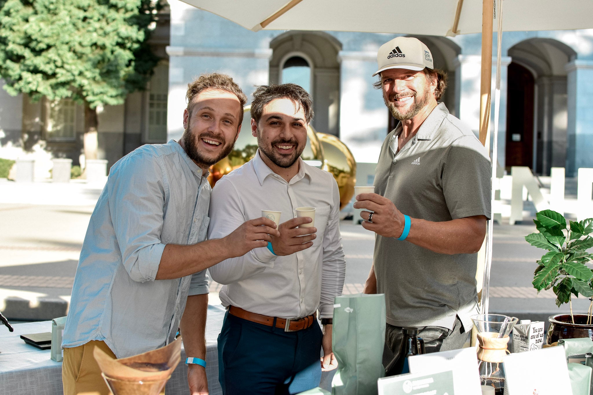 three men smile at camera holding coffee in hand