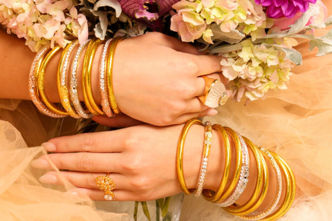 Women holding flowers while wearing Three Queens All Weather Bangles and Gold all weather bangles.