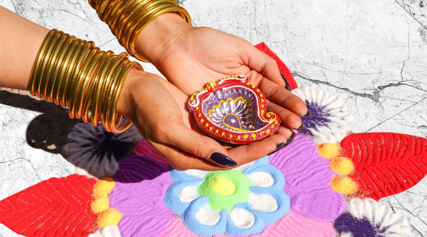 Woman holding oil Diya lamp wearing BuDhaGirl Gold All Weather Bangles, Colorful Diwali Rangoli | BuDhaBrief by BuDhaGirl 