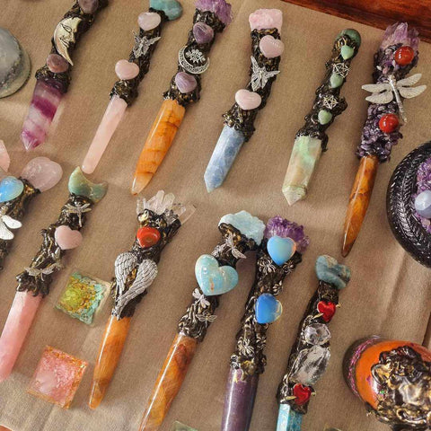 A collection of crystal wands of different colours made of clay and gemstones laying on a brown table