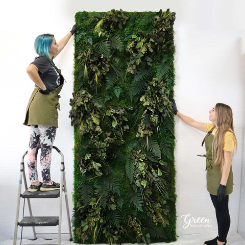 Two women with a moss and fern wall 