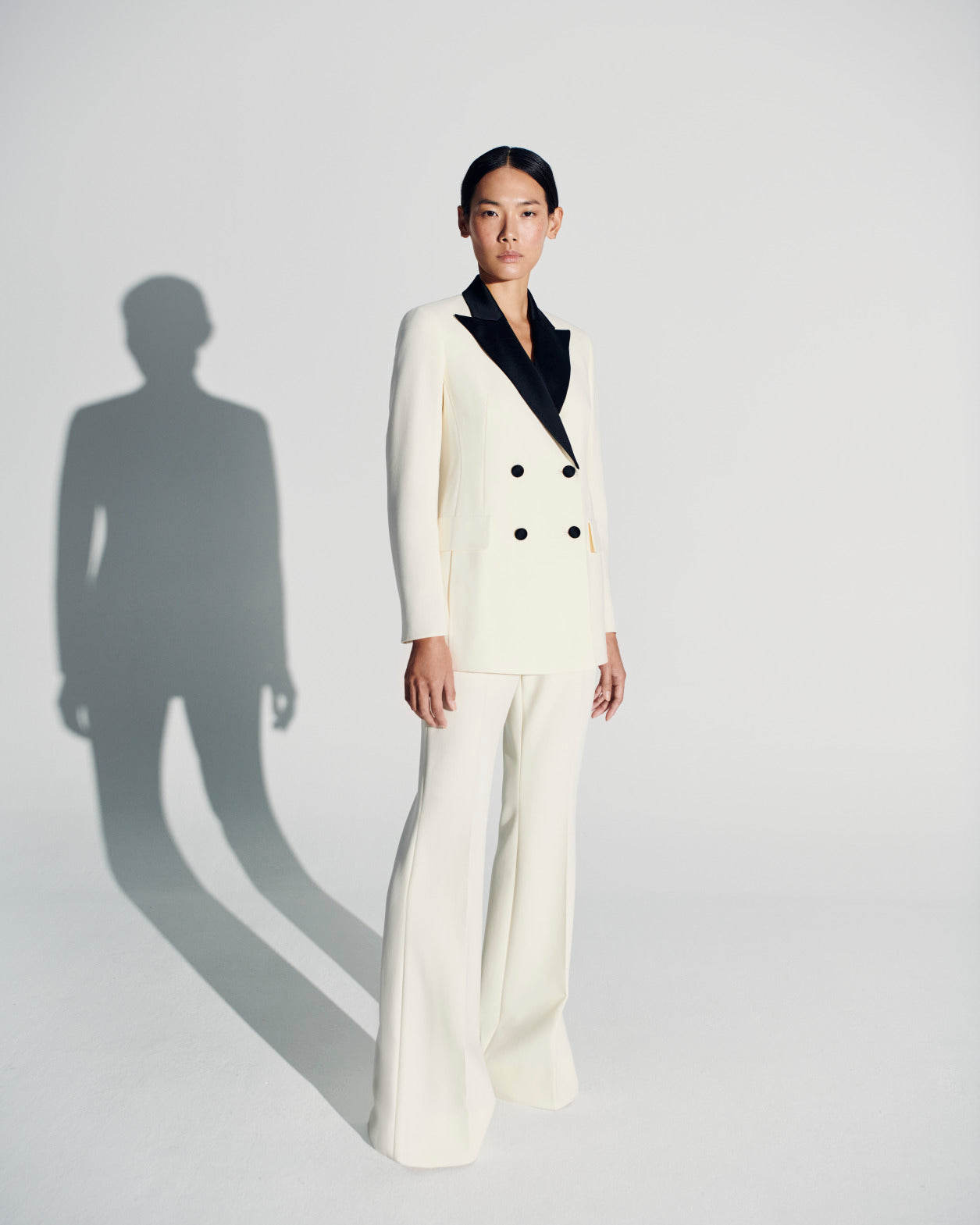 An Asian model poses in an elegant ecru pantsuit by Akris with a black collar.