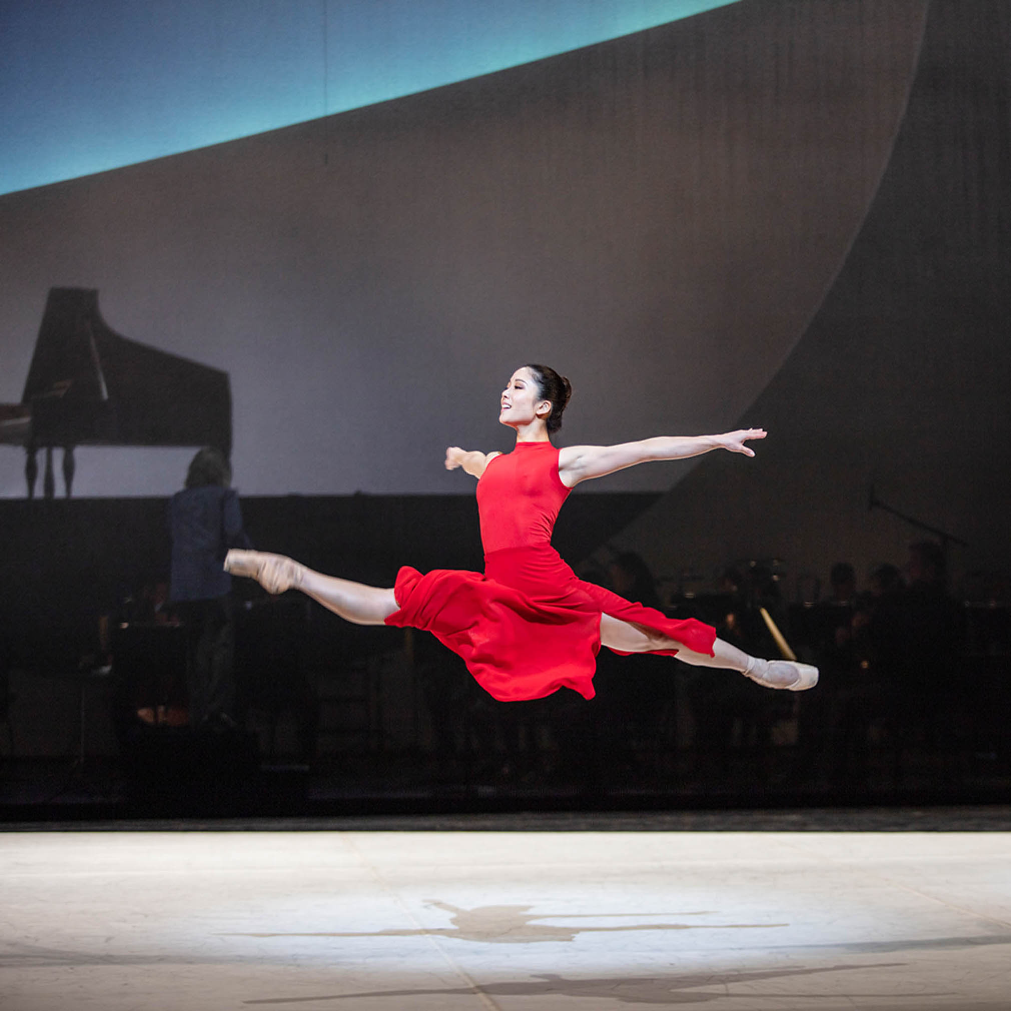 Ballerina der Hamburger Staatsoper flight nahezu schwerelos in der Luft in einem langen, roten Akris Kleid