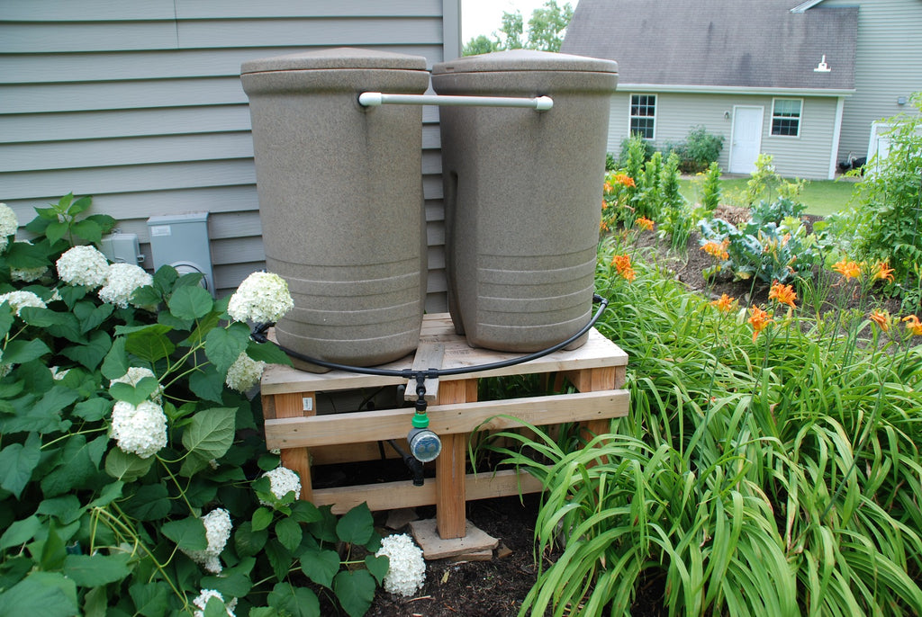 two gray rain barrels elevated on wood pallets in backyard garden