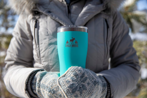 Woman in grey winter coat and knit mittens holding a Chilly Moose 20oz Killarney Tumbler in Southampton seafoam blue colour.