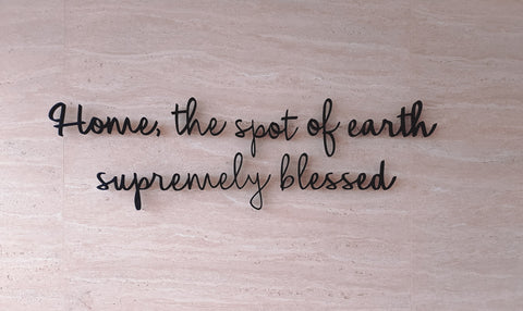 Home, the spot of earth supremely blessed, written in cursive on a wooden background.