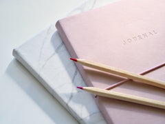 A set of notebooks with pencils lying across the top notebook.