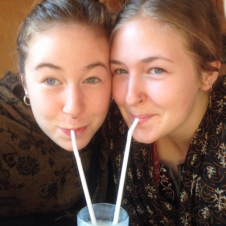 Two women smiling as they sip from the same drink with two straws