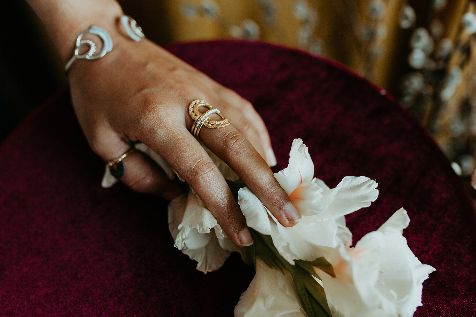 A hand touching a group of flowers and wearing assorted Twyla Dill rings