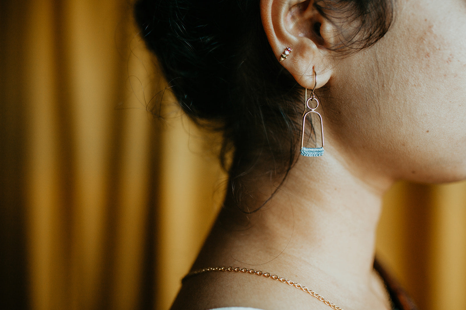 Close up side profile of a person, zoomed in on their ear, which is wearing a Twyla Dill Linnu Earring that is 14kt Gold-Plated and has Slate hand-crocheted lace