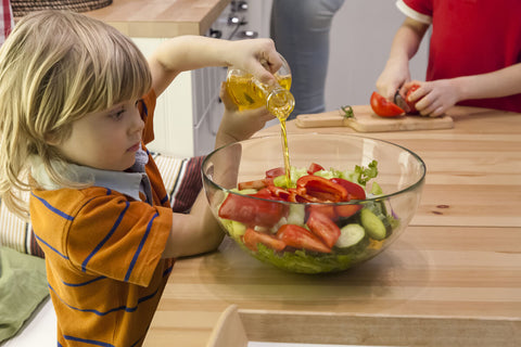 Little boy pouring oil into a bowl of salad