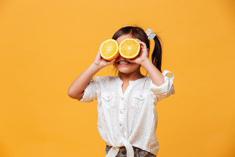 Immune boosters for kids: little girl covering her eyes with orange slices