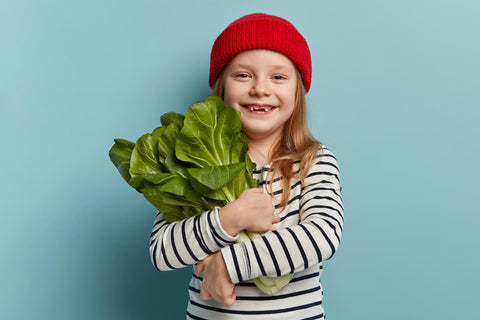 Iodine for kids: little girl hugging a bunch of green, leafy, vegetables