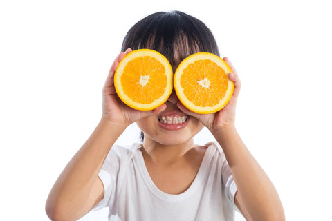 Vitamin C for kids: little kid holding an orange sliced in half in front of their eyes