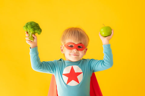 riboflavin for kids: little boy in superhero costume holding vegetables