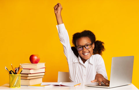 Omega 3 for kids: success concept - little girl with her arm raised while studying at her desk