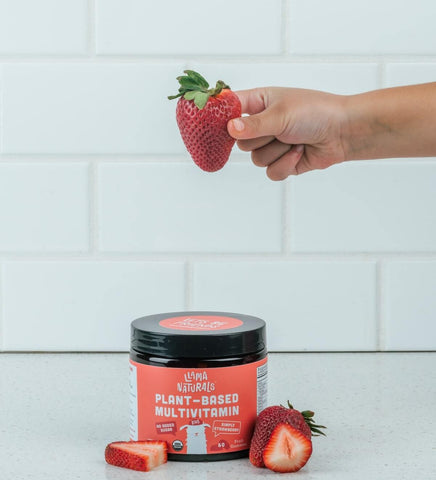 Person holding a strawberry on top of a jar or Llama Plant-Based Multivitamin