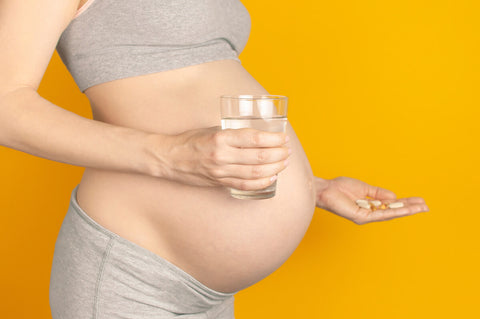 When should you start taking prenatal vitamins: pregnant woman holding a glass of water and various supplements