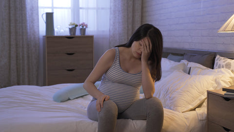 Tired pregnant woman sitting at the side of her bed