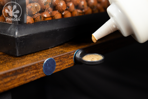 A small Pangea MicroDish magnetically mounted on a blue metal holding dot next to a second holding dot in front of a bioactive enclosure being filled with Pangea Crested Gecko Diet from a squeeze bottle..