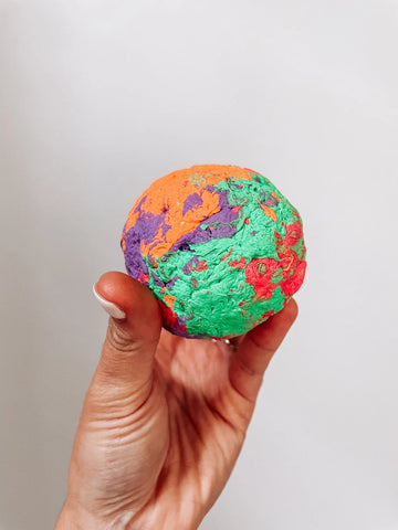 A multicolored, rubber dog ball is held up on a white background.