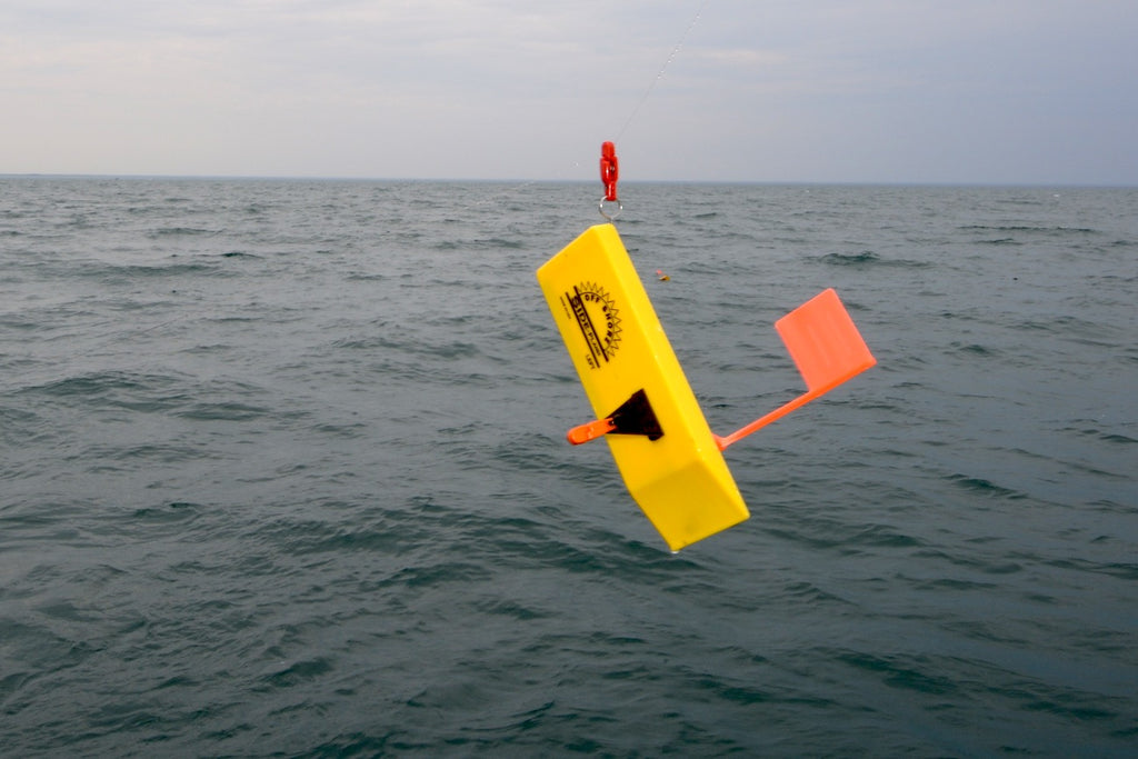 This in-line board is being fished in combination with segmented lead core line to “stealth troll” in clear water conditions. The line has tripped from the release on the tow arm and is being held in place on the line via a line clip at the back of the board. Rigged in this manner multiple boards can be stacked per side of the boat and fish reeled in without having to clear other board lines. 