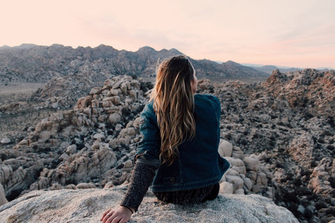 Woman sitting on rock overlooking a dessert view,travel skincare tips