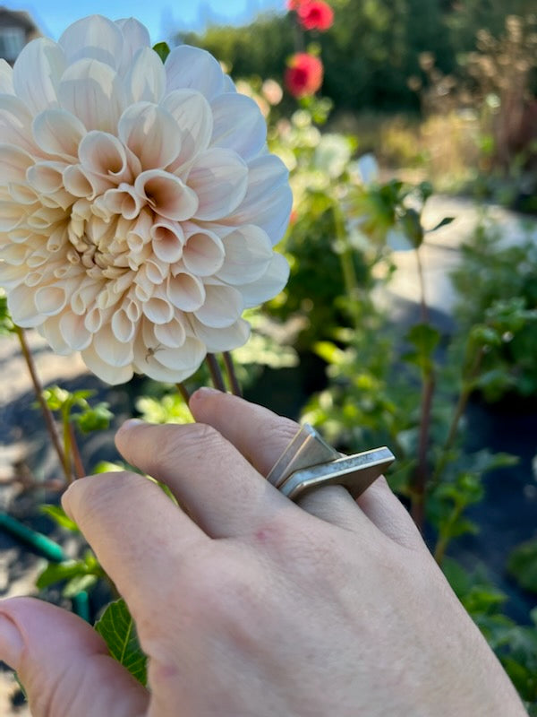 Two stackable angle top rings on a woman's finger in front of a beautiful flower