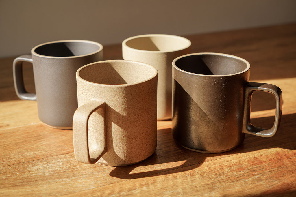 Hasami Porcelain mugs in natural and black on a wooden table.