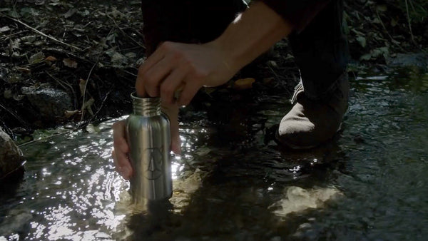 Steel bottle in stream collecting water