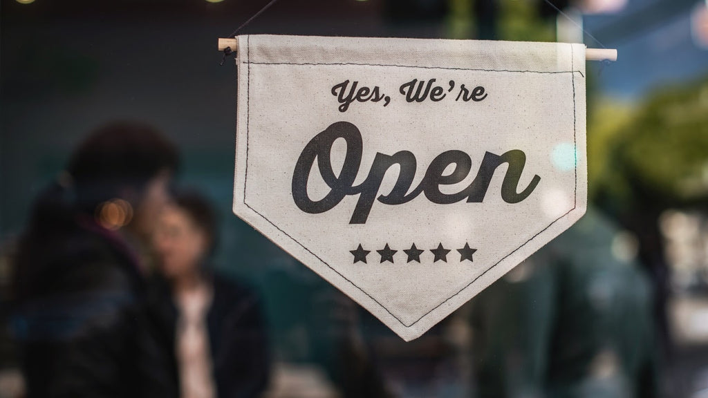 A small hanging sign on a glass door saying "We're open"