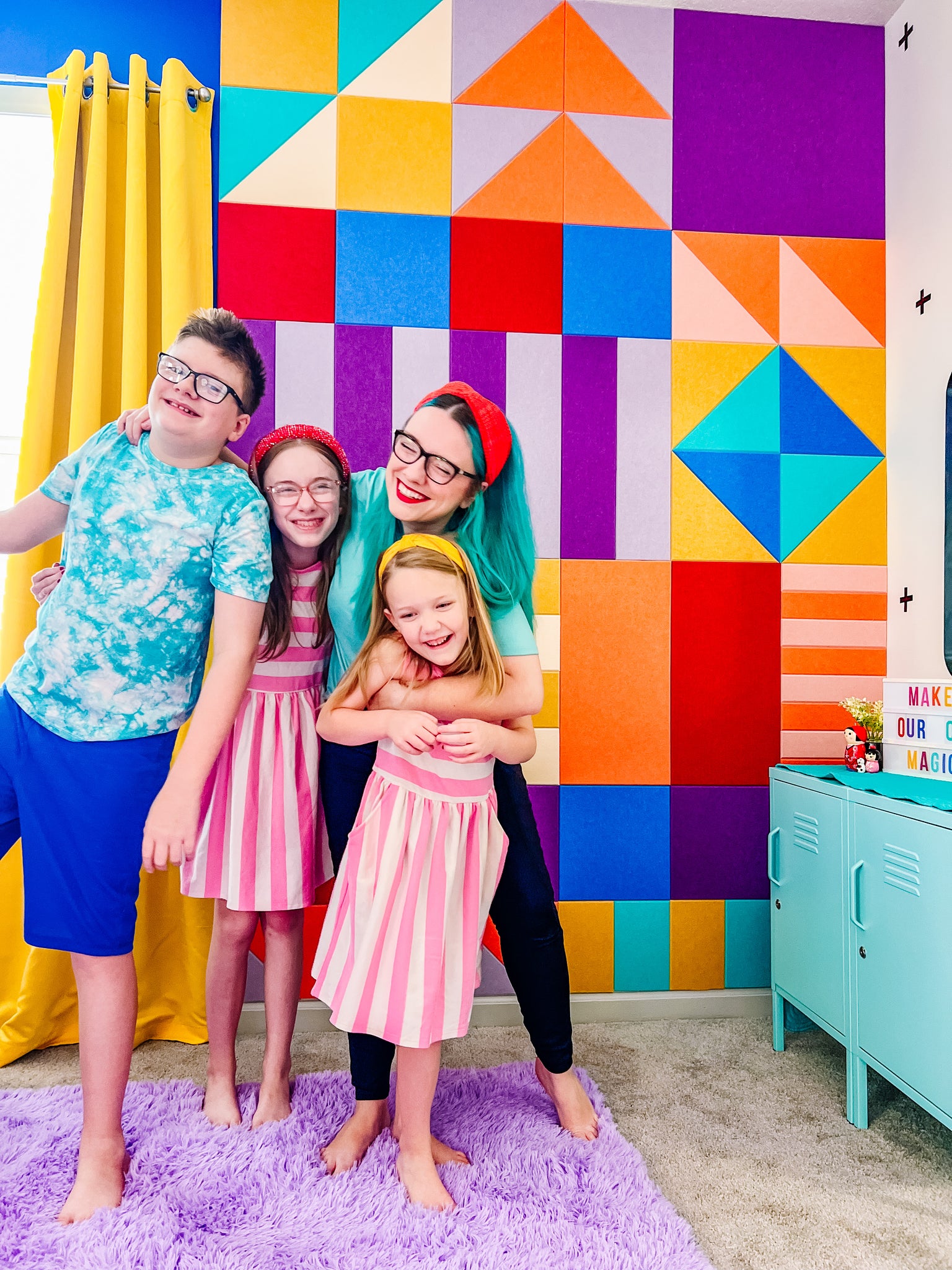 Mother hugging 3 smiling children in front of colorful Felt Right wall tiles.