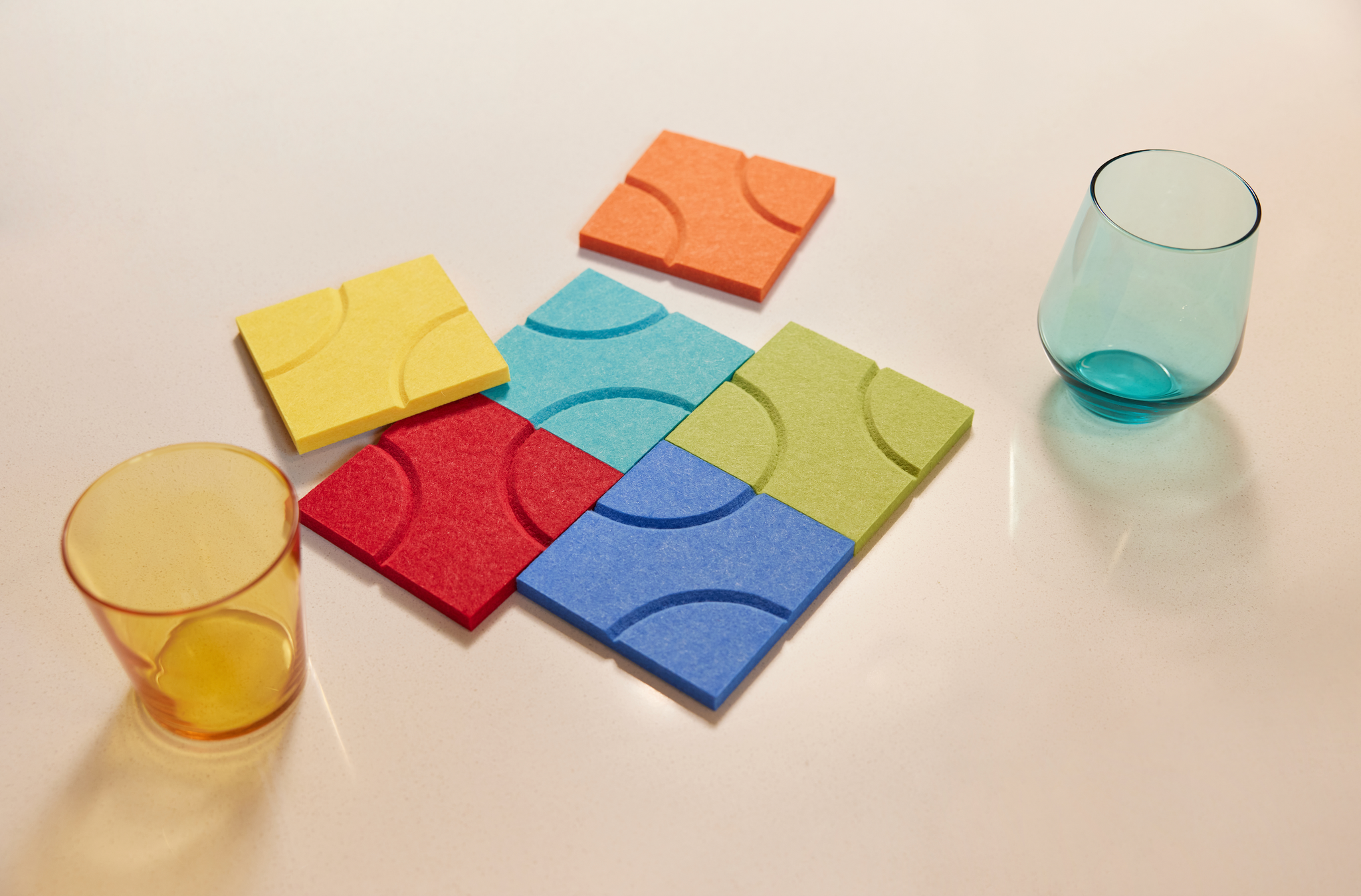 Rainbow colored coaster pack on countertop next to two cups.