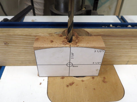 A drill press and fence drilling a 1/4" pilot hole with a brad point bit 1-1/4" deep into the fence