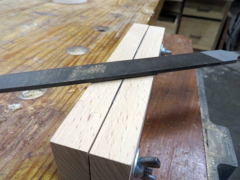 A single cut file laying on top of the vise on a wooden workbench