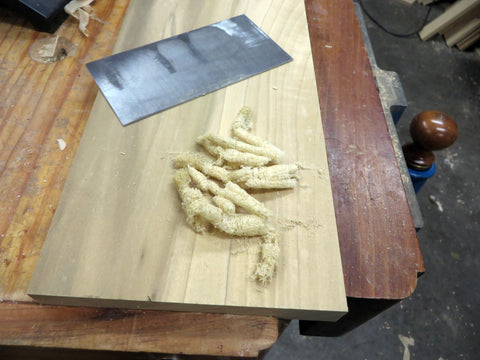 A scraper on a slab of wood with wood shavings