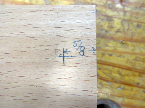 a pencil mark on a cut piece of hardwood marking 5/8" from the edge of the wood on a wooden workbench