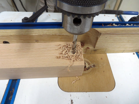 A drill press drilling through the pieces of cut hardwood that are stuck together