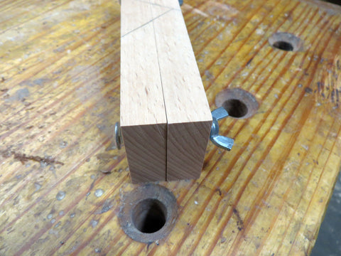 The two pieces of cut hardwood together with a long carriage bolt through them on a wooden workbench